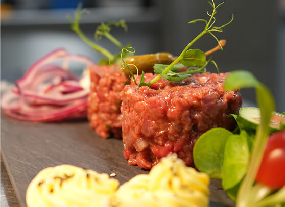 Steak Tartar mit Beilagen auf dunklem Brett.