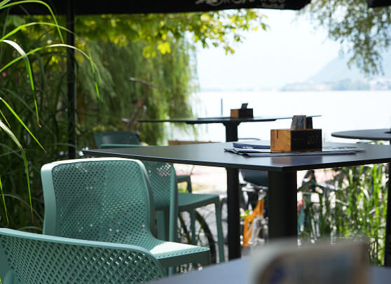 Grüne Stühle und schwarze Tische auf einer Terrasse am See.