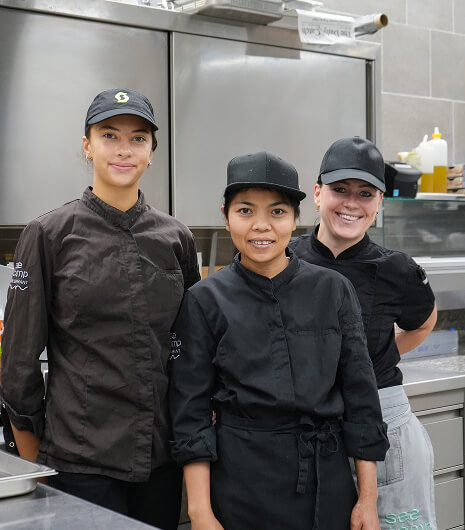 Drei lächelnde Küchenmitarbeiterinnen in schwarzen Uniformen.