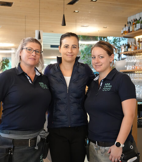 Drei Frauen in Uniformen lächeln in Restaurantkulisse.