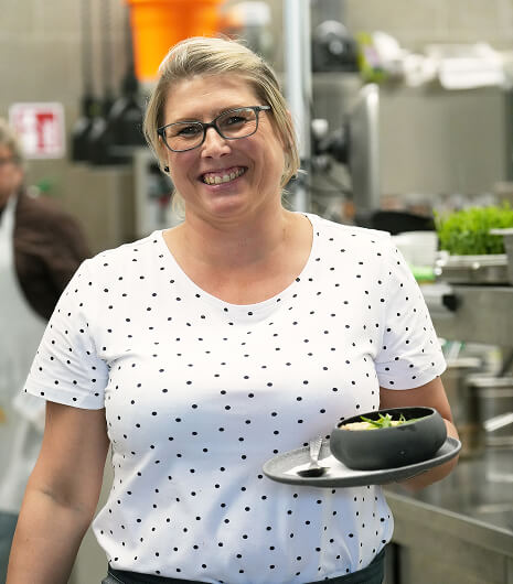 Lächelnde Frau hält Schale mit Gericht in Küche.