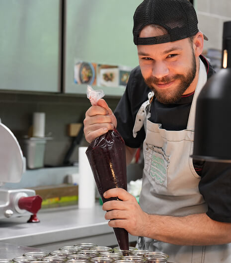 Mann füllt dunkle Masse mit Spritzbeutel in Behälter.
