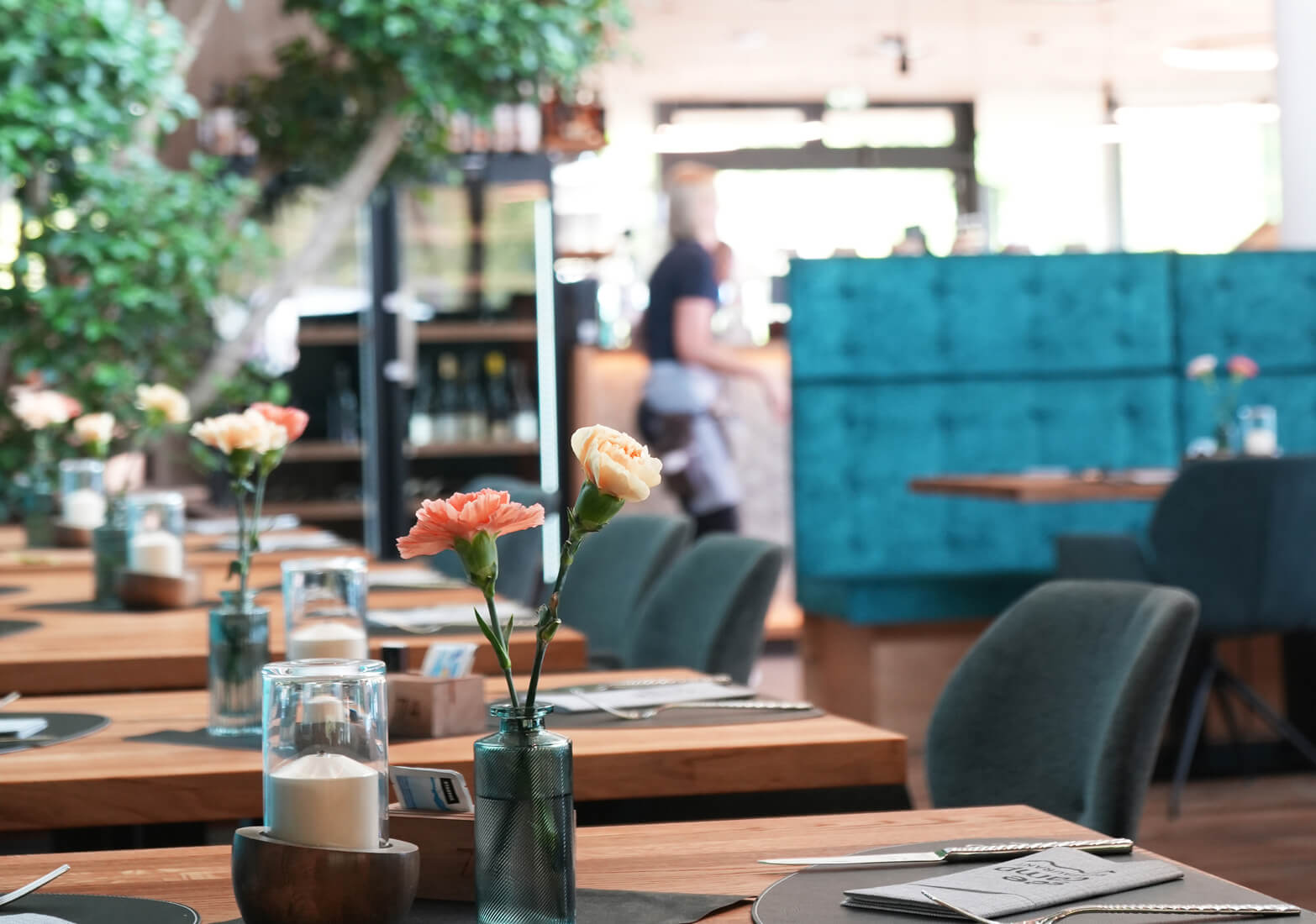 Restaurant mit gedeckten Holztischen, Blumen und Kerzen.