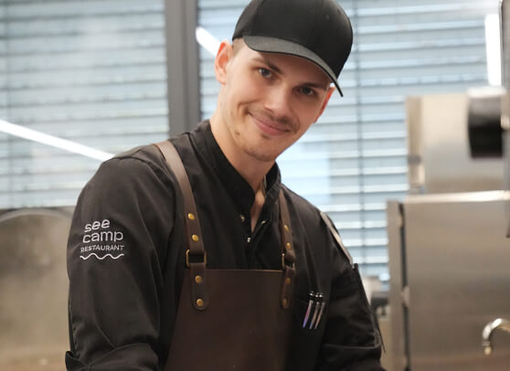 Mann in schwarzer Restaurantuniform und Lederschürze lächelt.