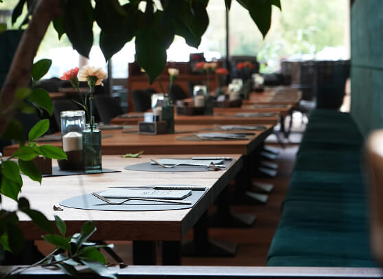 Reihen von gedeckten Restauranttischen mit Blumen und grünen Bänken.