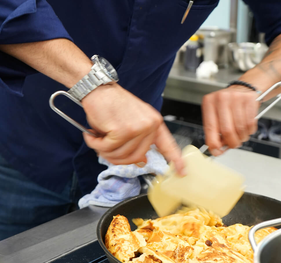 Koch zerkleinert Kaiserschmarrn in Pfanne.