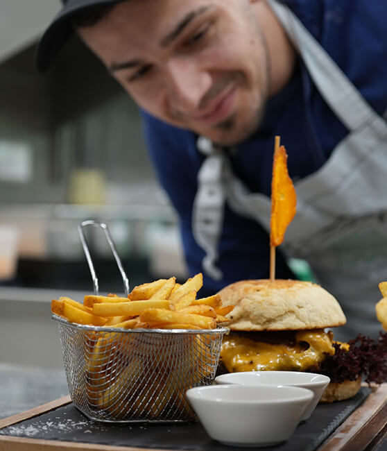 Koch betrachtet Burger, Pommes und Saucenschalen.