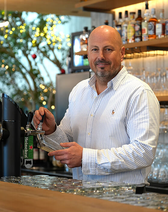 Mann zapft Bier an Bar und lächelt.